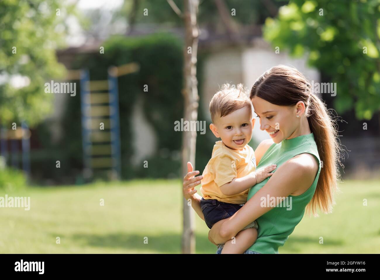 madre allegra e giovane che tiene in braccio figlio toddler che sporge la lingua Foto Stock