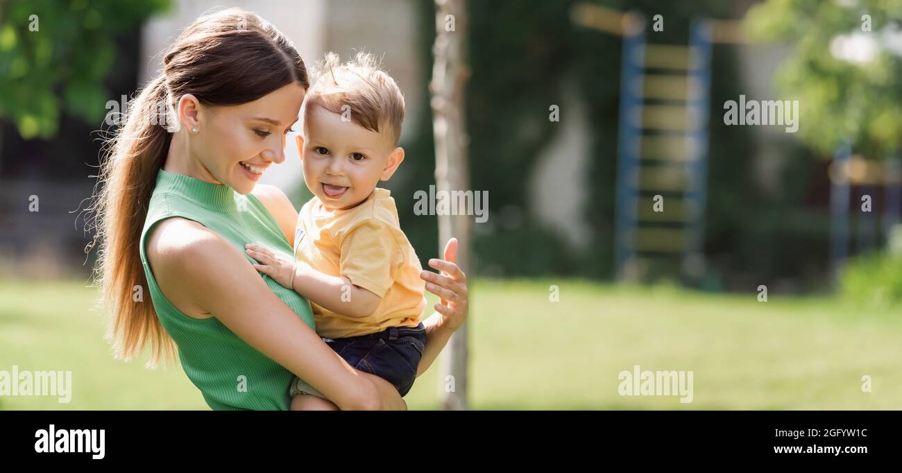 mamma allegra e giovane che tiene in braccio figlio toddler che sporge lingua, banner Foto Stock