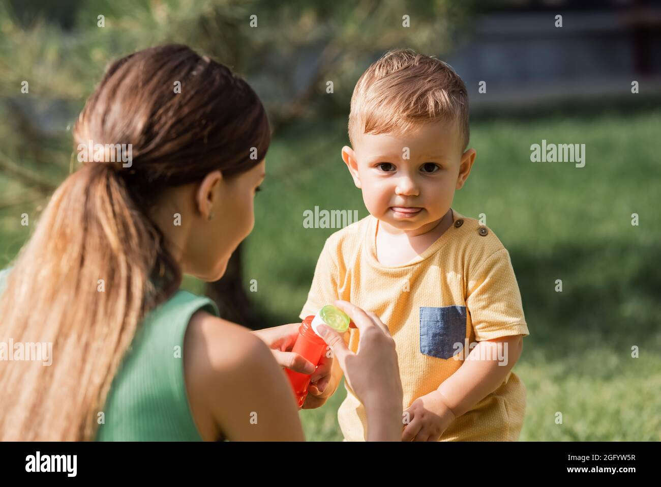 la madre offuscata che tiene la bottiglia e la bacchetta della bolla vicino al bambino fuori Foto Stock
