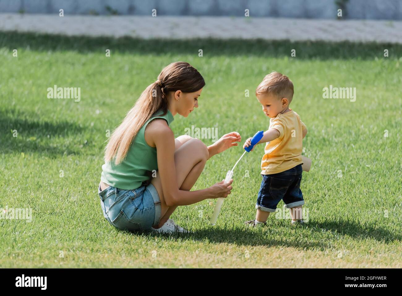 giovane madre che tiene la bottiglia della bolla del sapone vicino il figlio del toddler sull'erba Foto Stock