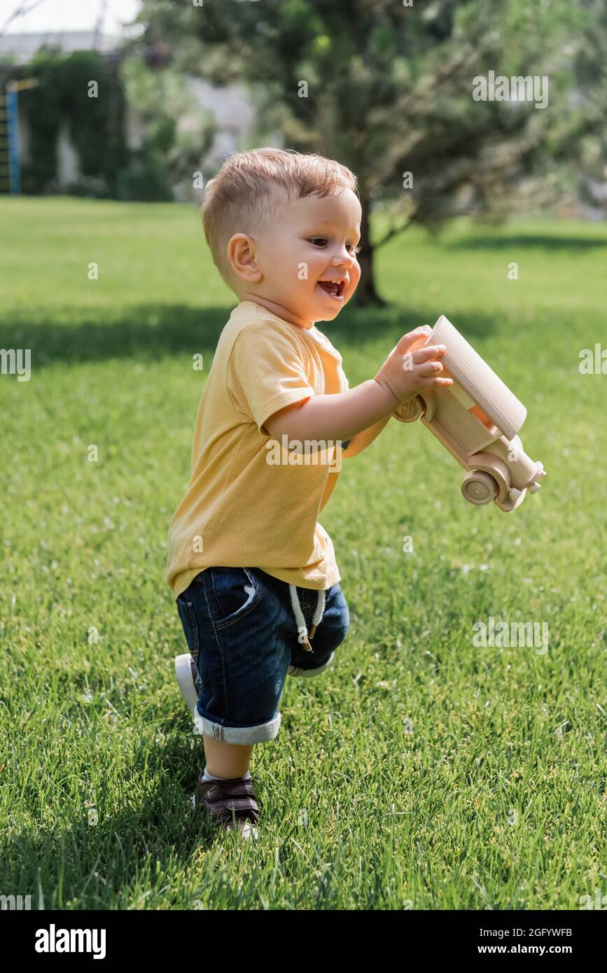 l'intera lunghezza del bambino felice con l'automobile di legno del giocattolo in piedi sull'erba verde Foto Stock