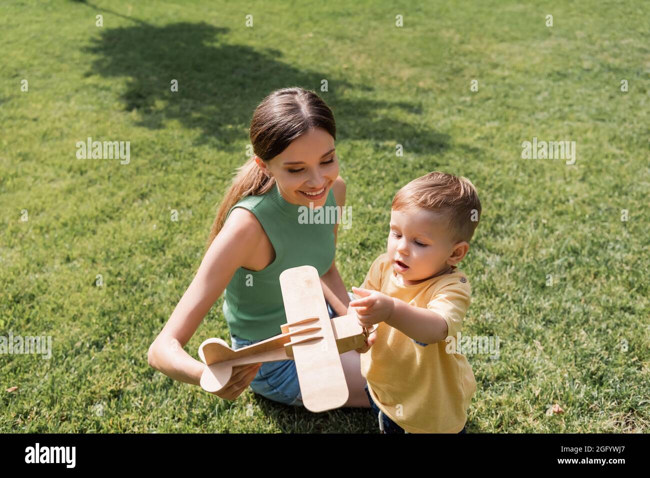 madre sorridente che tiene il biplano giocattolo vicino al figlio del bambino sull'erba Foto Stock