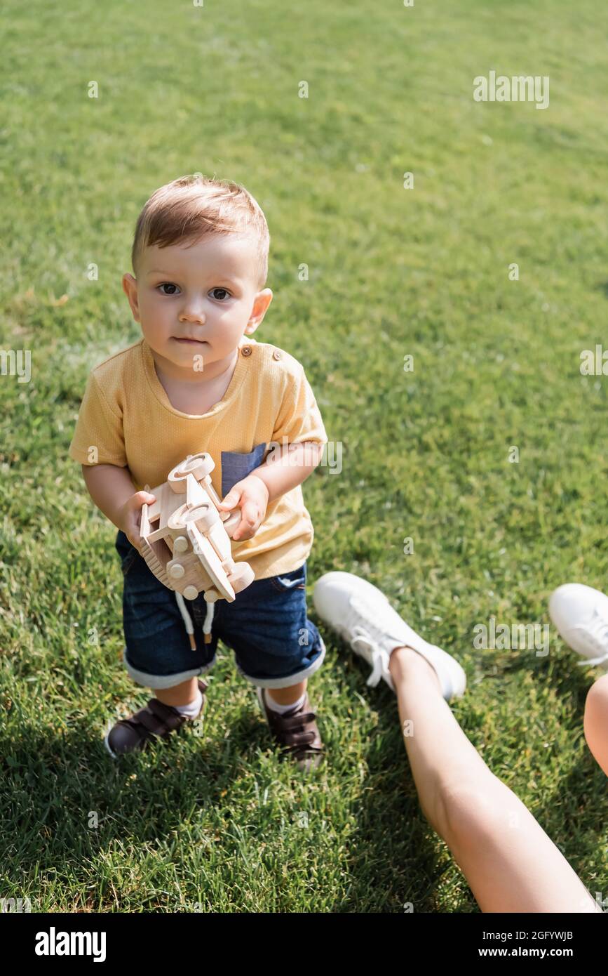 ragazzo del toddler in piedi sull'erba e tenendo l'automobile del giocattolo vicino alla madre Foto Stock