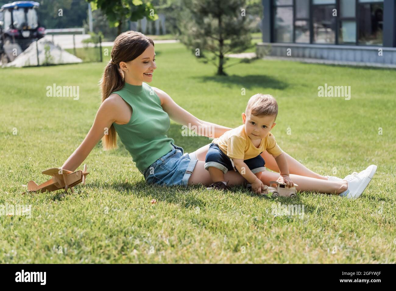 madre giovane felice che guarda il figlio allegro del toddler che gioca sull'erba Foto Stock
