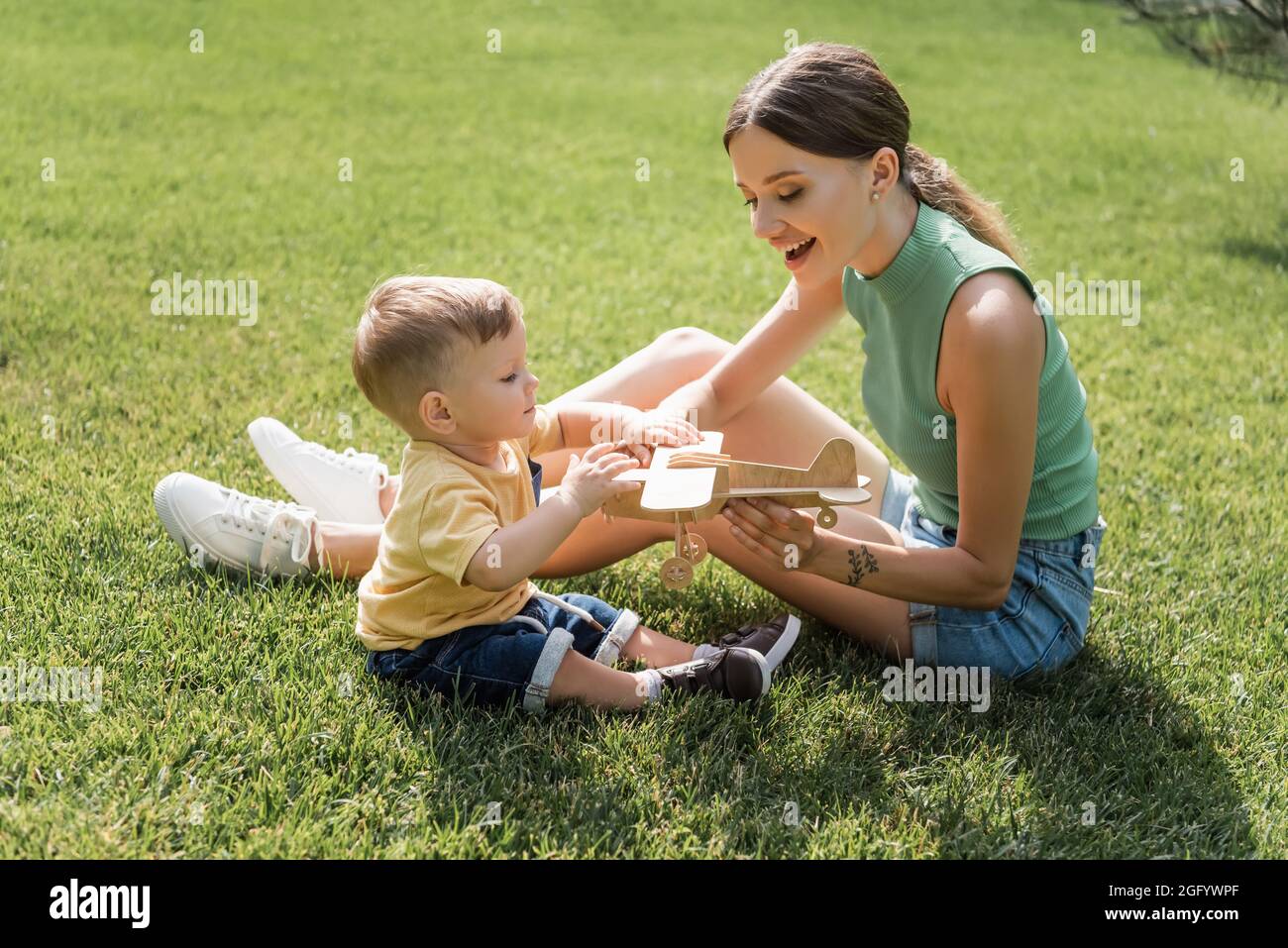 madre allegra che tiene il biplano giocattolo vicino al figlio del bambino sull'erba Foto Stock