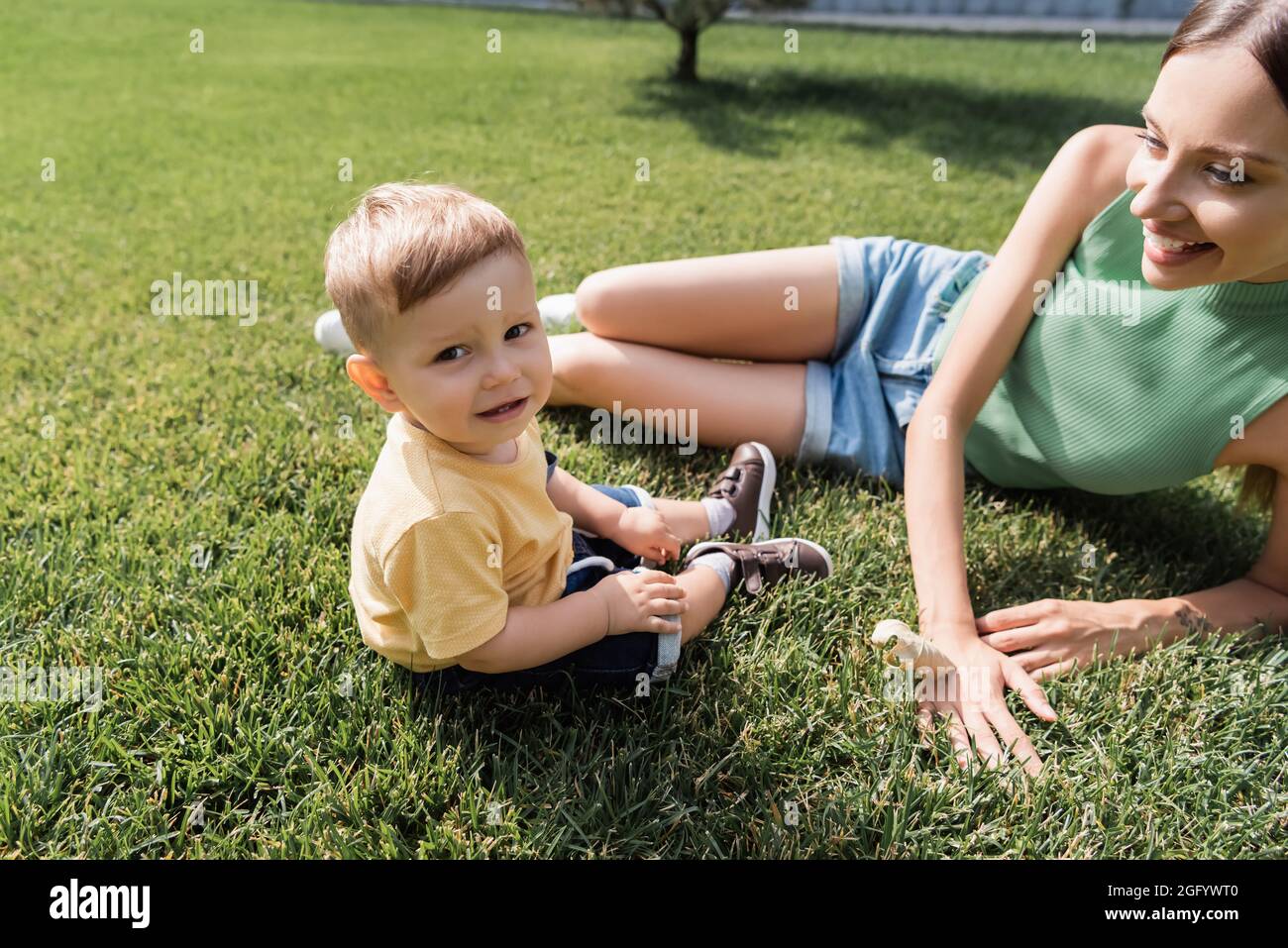 madre giovane felice che guarda il figlio allegro del toddler sull'erba Foto Stock