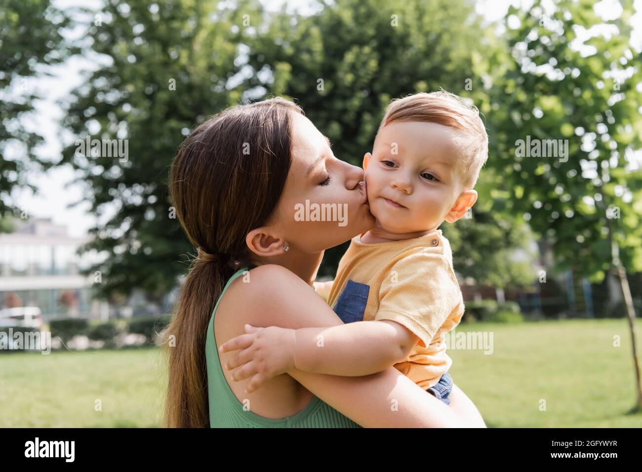 giovane madre che tiene le braccia e bacia il figlio del bambino Foto Stock