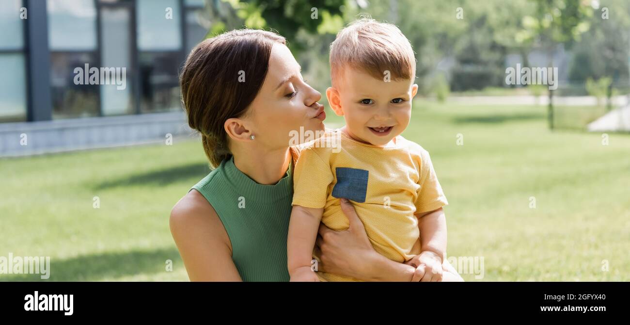 giovane madre baciando felice figlio del bambino fuori, bandiera Foto Stock