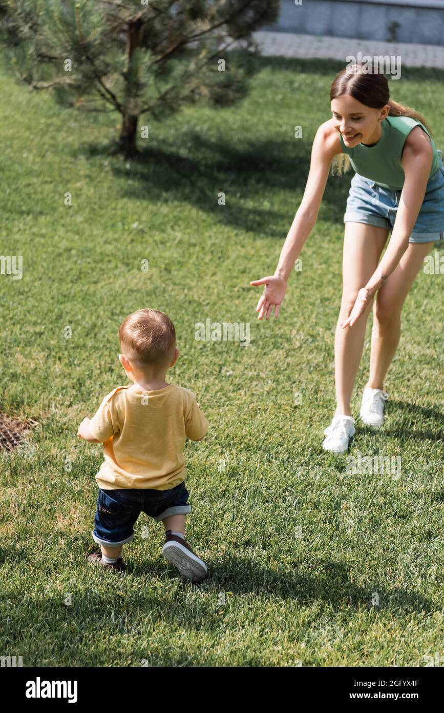 madre allegra con le mani distese in piedi sull'erba e raggiungendo il figlio del bambino fuori Foto Stock