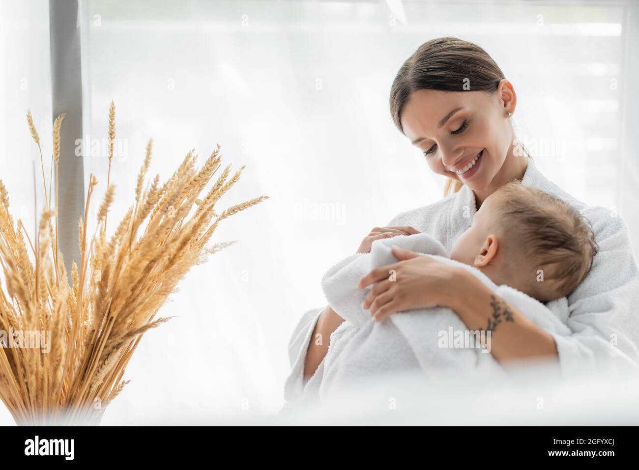 felice madre che abbraccia il bambino che dorme in accappatoio Foto Stock