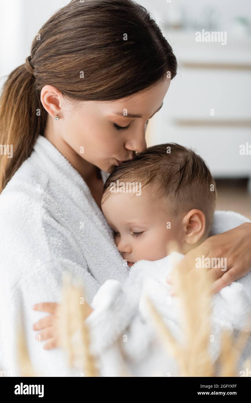 giovane madre che bacia la testa del bambino in accappatoio Foto Stock