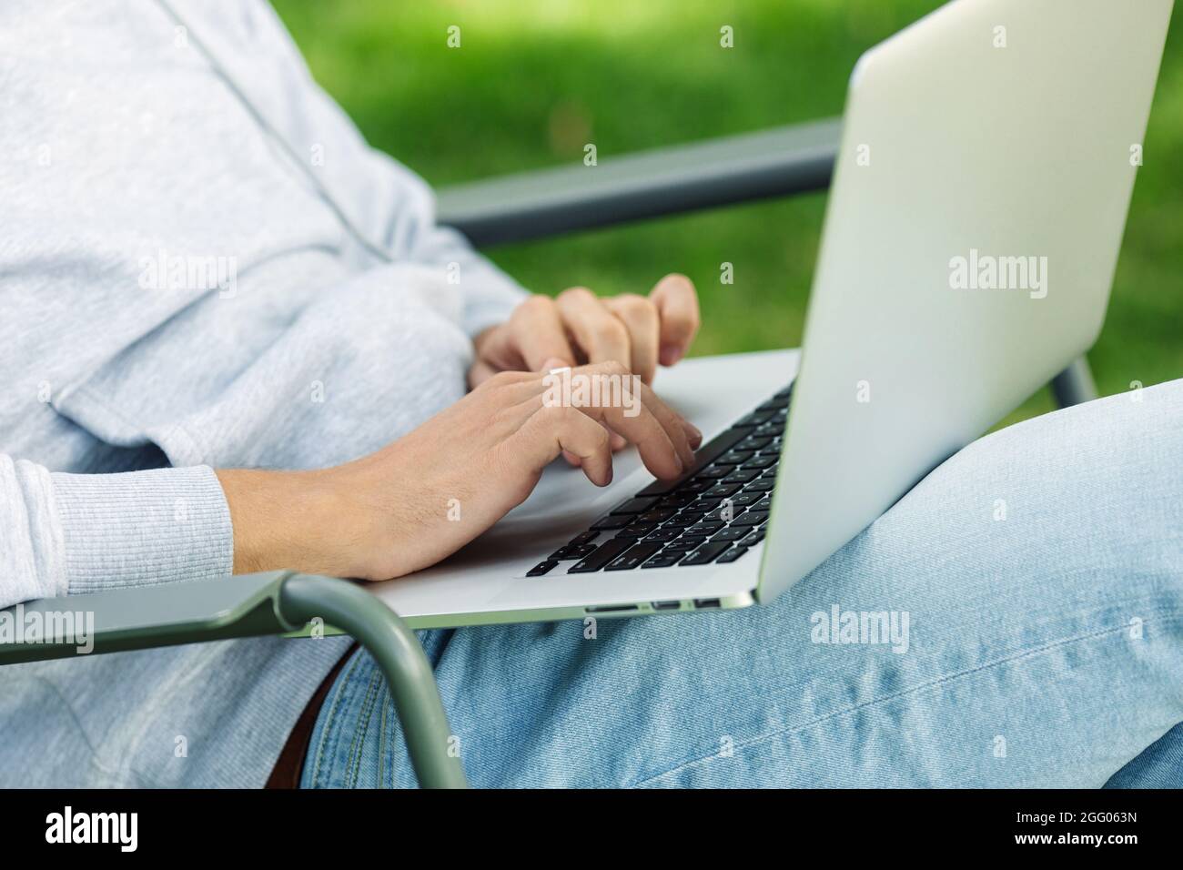 Primo piano braccia di blogger uomo con computer portatile che lavora all'aperto in giardino, seduto su sedia. Foto Stock