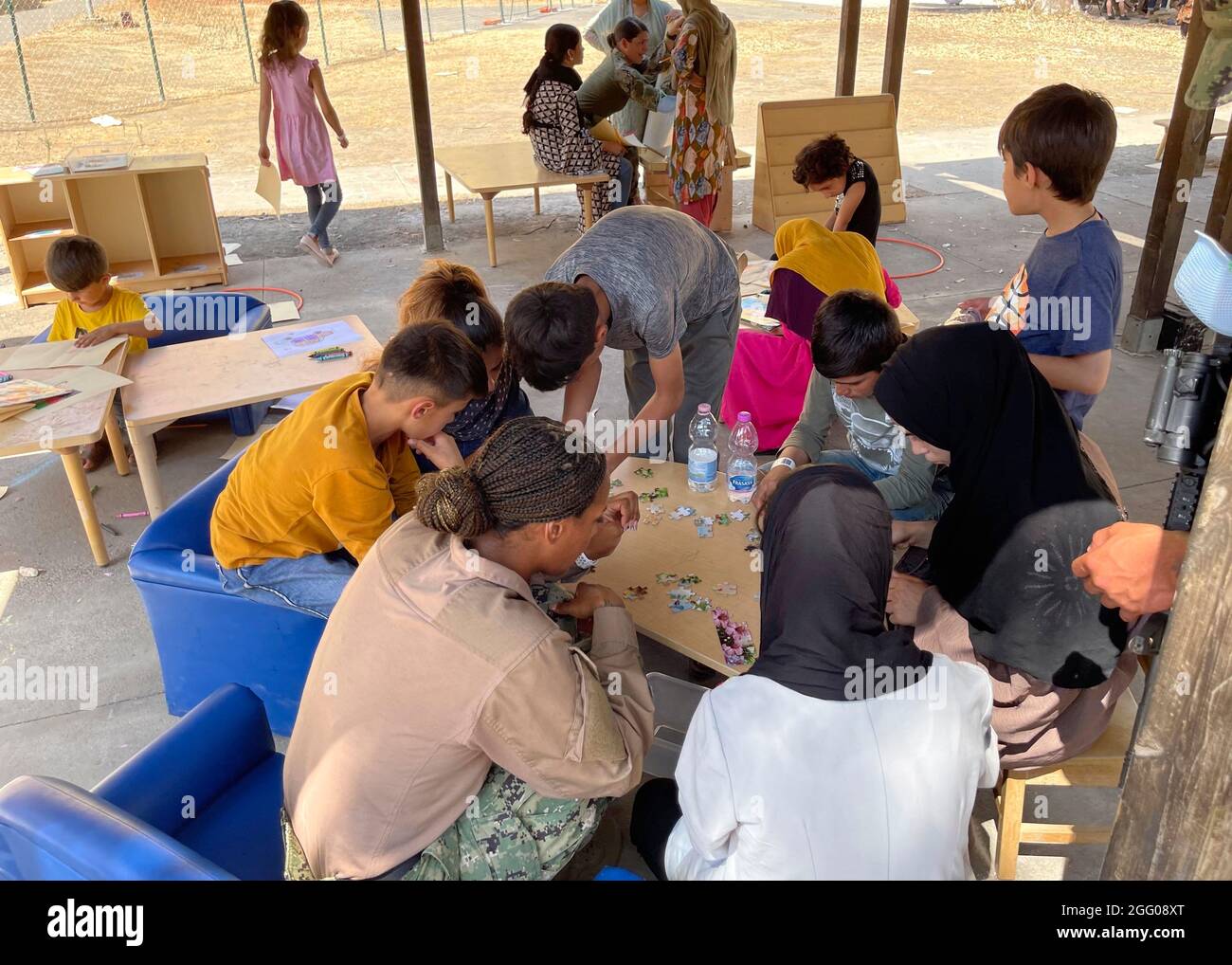 Sigonella, Italia. 24 agosto 2021. Un marinaio della Marina degli Stati Uniti si unisce agli evacuati afghani nell'assemblaggio di un puzzle alla Stazione aerea navale di Sigonella il 24 agosto 2021 a Sigonella, Italia. NAS Sigonella fornisce alloggio temporaneo per gli evacuati dall'Afghanistan come parte dell'operazione Rifugi Alleati. Credit: Planetpix/Alamy Live News Foto Stock