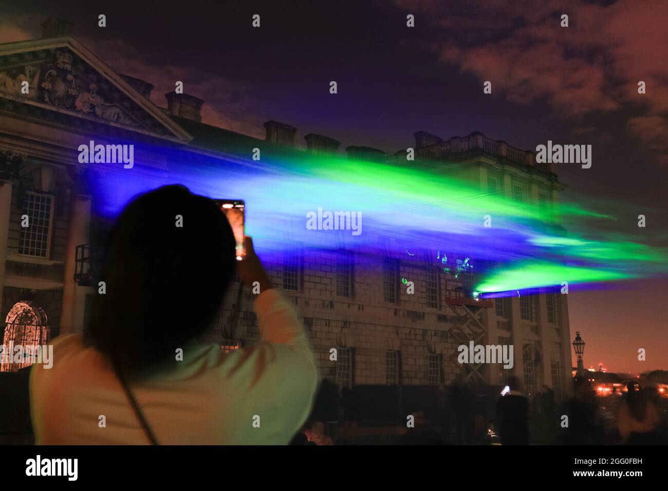 Greenwich, Londra, Regno Unito. 27 ago 2021. Un visitatore scatta foto dello spettacolo. Nella sua serata ufficiale di lancio pubblico, 'Borealis' di Dan Archer illumina i cieli sopra l'Old Royal Naval College nel Royal Borough di Greenwich. 'Borealis' è una riproduzione ipnotizzante dell'aurora boreale nel cielo. Fa parte dell'annuale Greenwich and Docklands Festival, che si terrà dal 27 agosto all'11 settembre 2021. Credit: Imagplotter/Alamy Live News Foto Stock