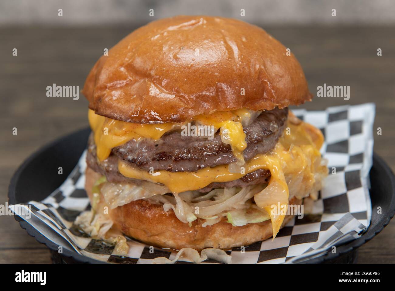 Un doppio cheeseburger alto con ingredienti e formaggio che si sciolgono dai lati per un pasto appetitoso. Foto Stock