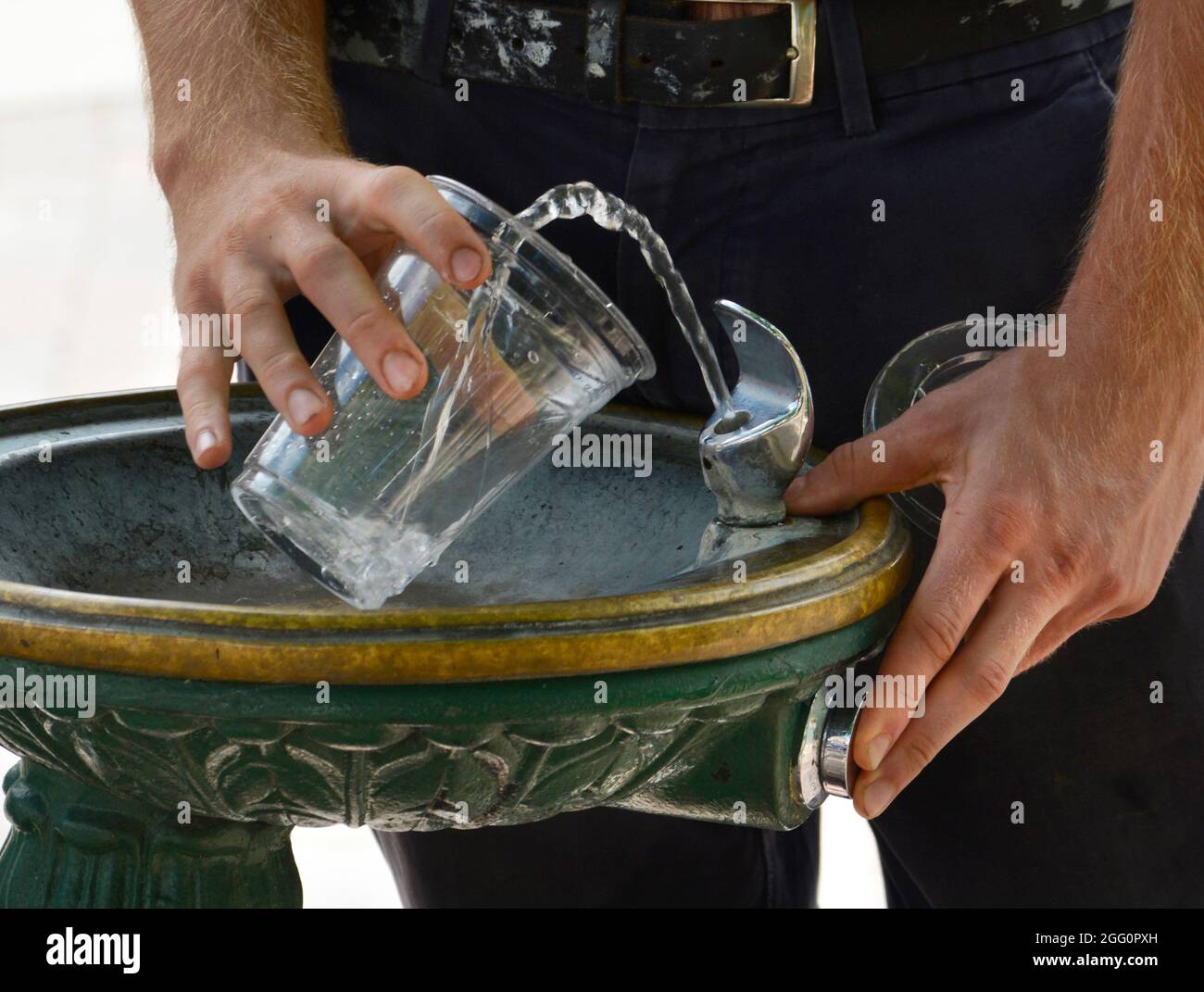 Un uomo riempie un vetro di plastica con acqua presso una fontana pubblica a Santa Fe, New Mexico. Foto Stock