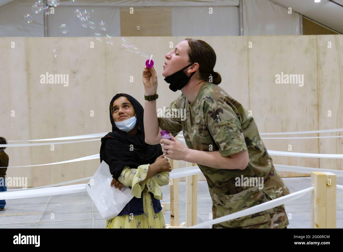 Un soldato della Guardia Nazionale dell'Esercito degli Stati Uniti con la Task Force Spartan, il Centro dell'Esercito degli Stati Uniti, intrattiene una ragazza afghana con le bolle mentre attende in-process a Camp Buehring, Kuwait, 23 agosto 2021. I soldati dell'esercito degli Stati Uniti continuano a lavorare con i loro compagni di squadra del comando centrale degli Stati Uniti e del Dipartimento di Stato per sostenere gli sforzi di evacuazione dell'Afghanistan con trasporto, sicurezza, logistica e assistenza medica nelle sedi in Kuwait. (STATI UNITI Esercito foto di 1 Lt. James Mason) Foto Stock