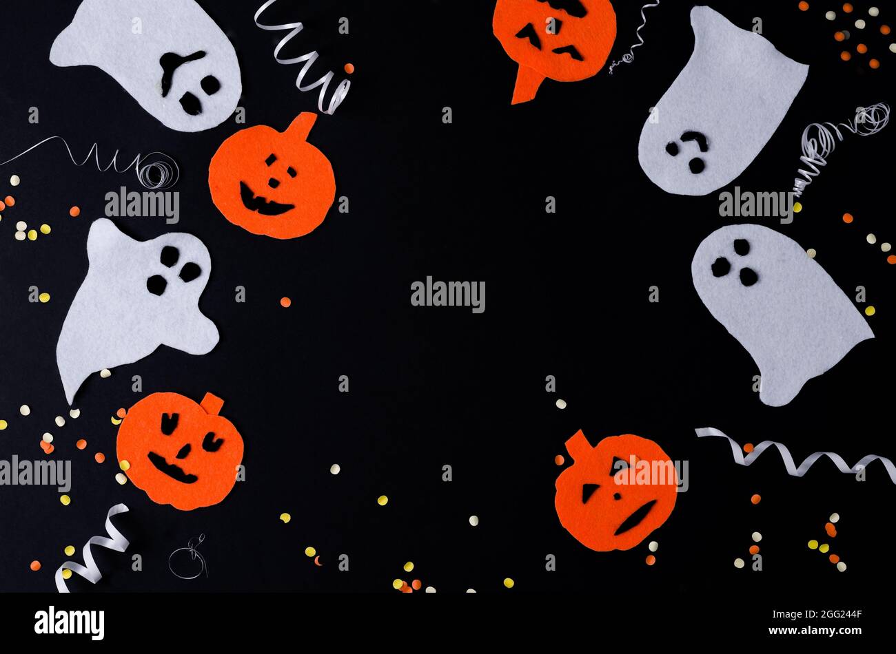 Sfondo nero festivo su Halloween. Fantasmi bianchi e zucche arancioni con serpentina giacciono su uno sfondo nero, spazio di copiatura, layout nero Foto Stock