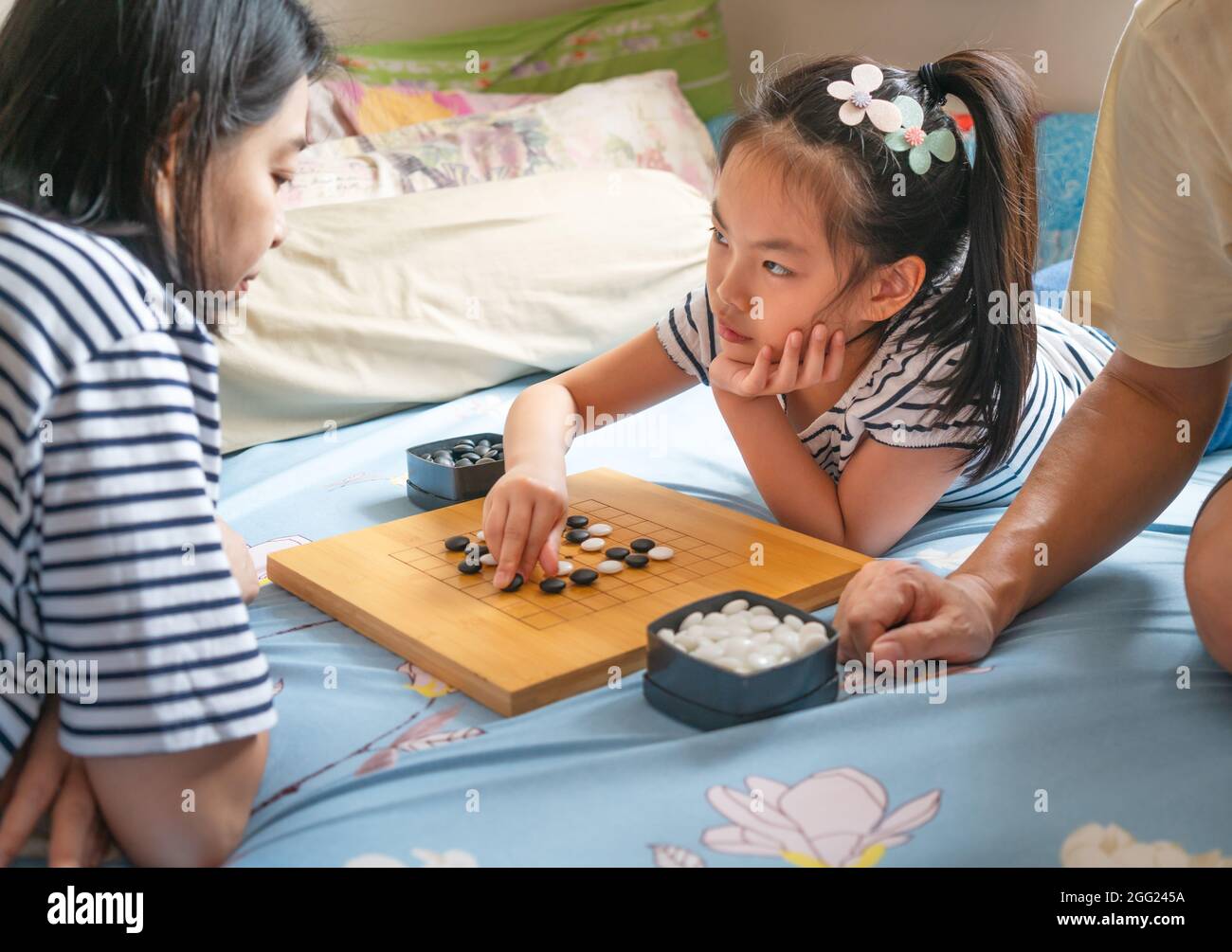 Ragazza carina asiatica bambino che gioca Go o cinese tradizionale gioco da tavolo a letto con la madre, utilizzare pietre bianche e nere per giocare, ragazza guardando volto avversario. Foto Stock
