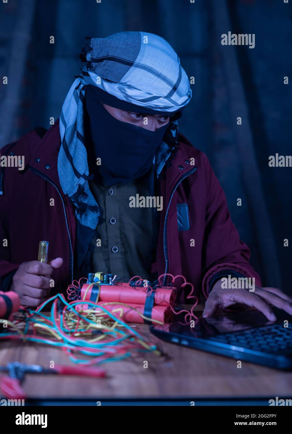 Militante con copertina apprendimento timer bomba fare con Dynamite guardando il portatile di notte. Foto Stock