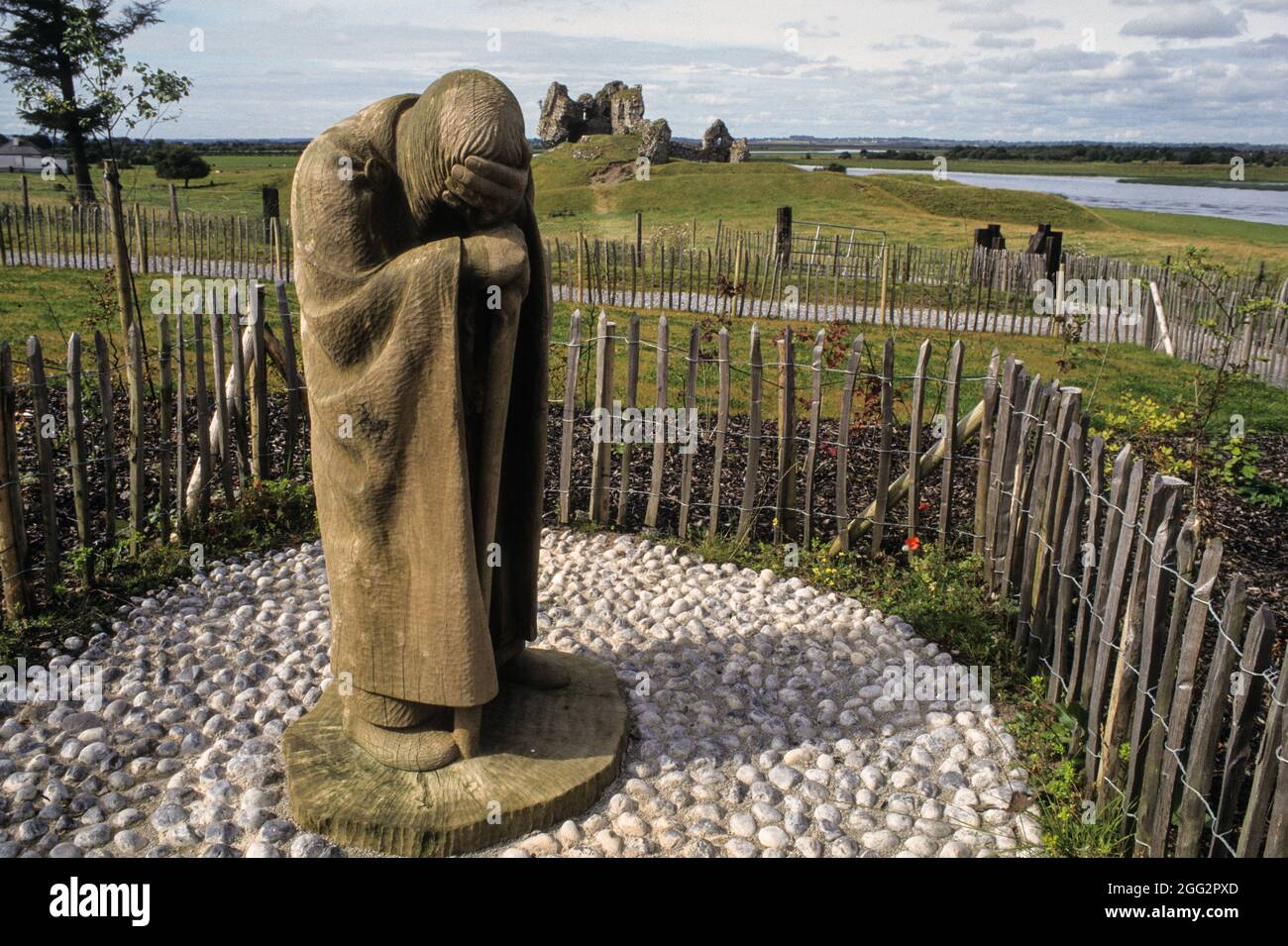 Statua di un pellegrino solitario sul terreno del monastero di Clonmacnoise con il castello medievale in rovina sullo sfondo sulle rive del fiume Shannon Foto Stock