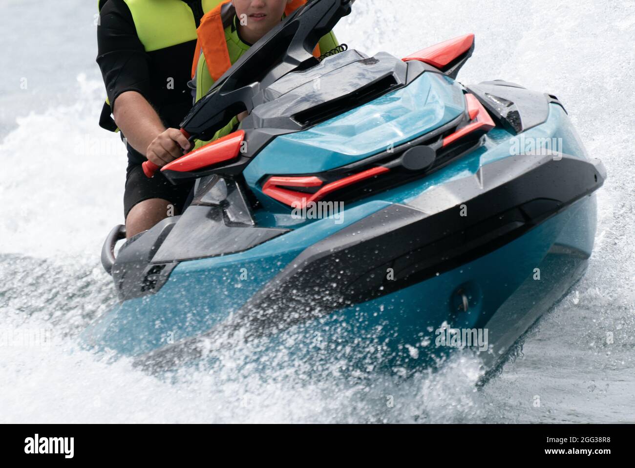 Hel, Polonia - 08.01.2021: Primo piano colpo frontale di uomo e ragazzo in giubbotti di vita a cavallo veloce su uno scooter d'acqua con un sacco di goccioline che volano attraverso Foto Stock