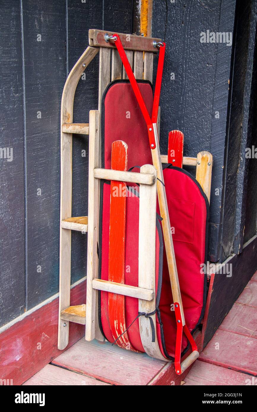 Legno e tela rossa neve slitta propped contro il muro su polveroso retro portico fuori stagione. Foto Stock