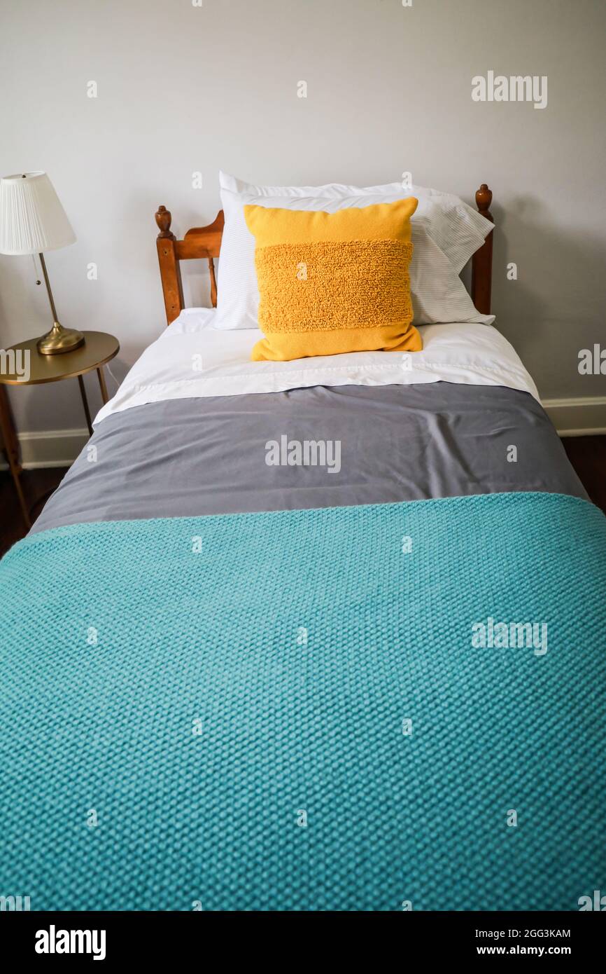 Una camera da letto con un letto singolo con copriletto color turchese e grigio e cuscino decorativo giallo Foto Stock