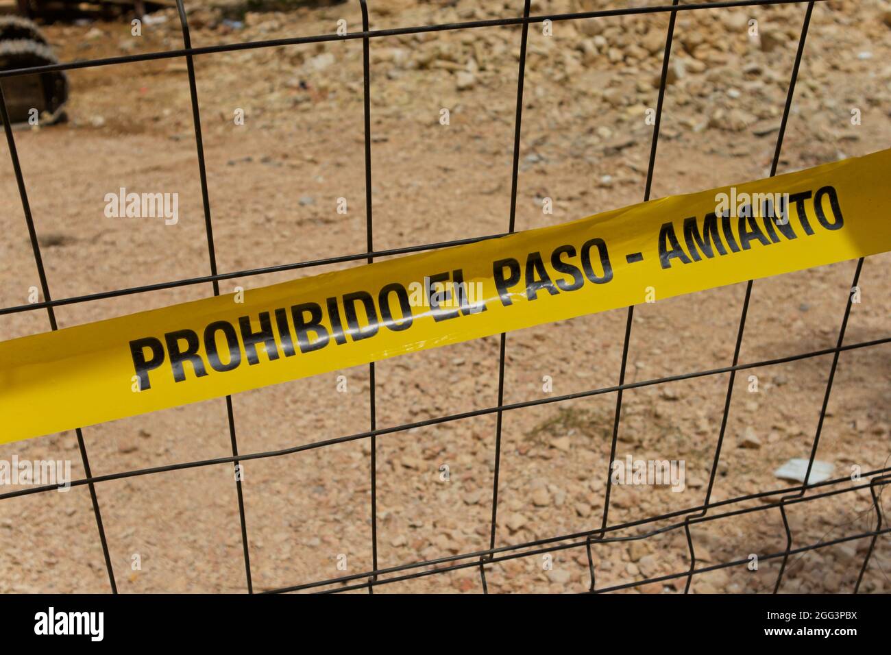 Primo piano di un nastro giallo che avverte della presenza di amianto in un'area urbana e che impedisce ai passanti di uscire dal cantiere con la tex Foto Stock