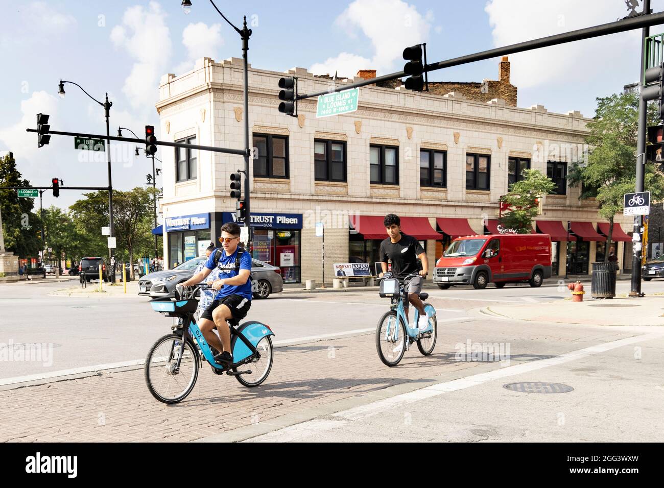 Due giovani uomini in bicicletta condividono biciclette attraversare Blue Island Avenue a Loomis Street nel quartiere Pilsen di Chicago, Illinois, USA. Foto Stock