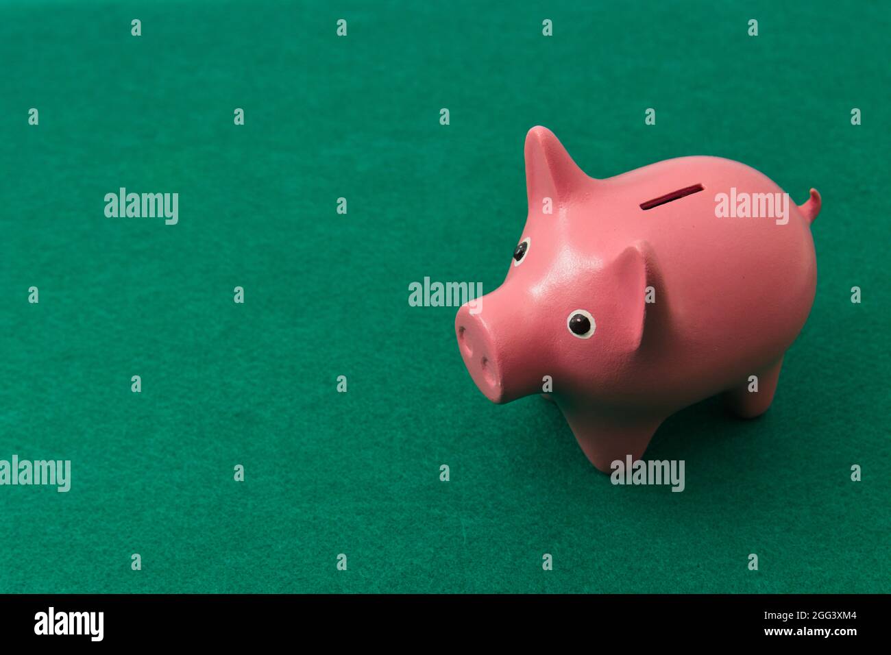 Primo piano di una banca piggy su un tavolo con un tappeto di gioco di bordo verde con spazio di copia a sinistra Foto Stock
