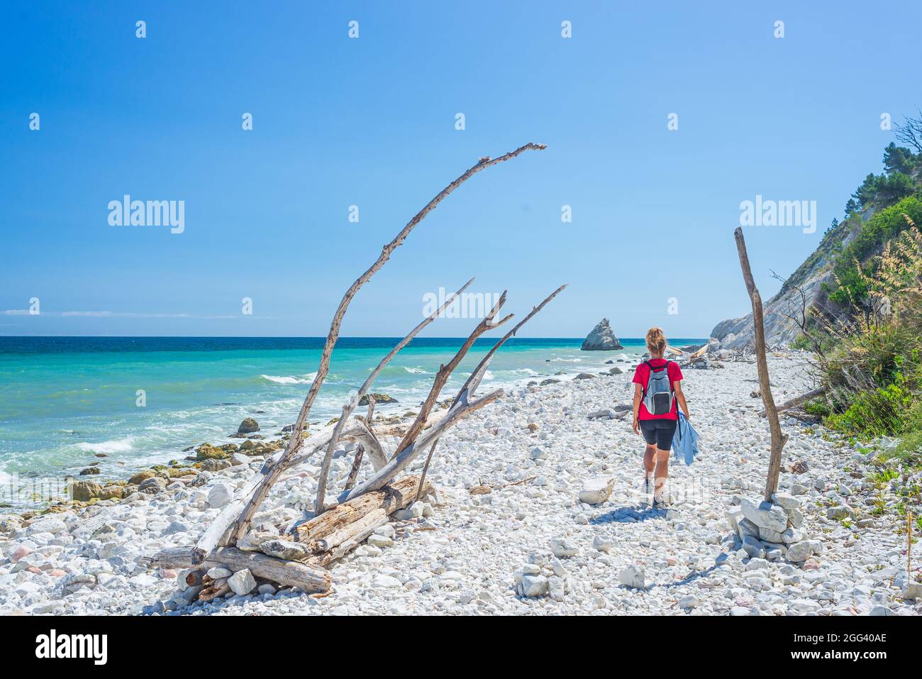 Donna che cammina sulla spiaggia italiana. Linea costiera Conero irregolare, spiaggia di ciottoli, acqua turchese gente reale, vista posteriore, giorno di sole, vacanza in Italia Foto Stock