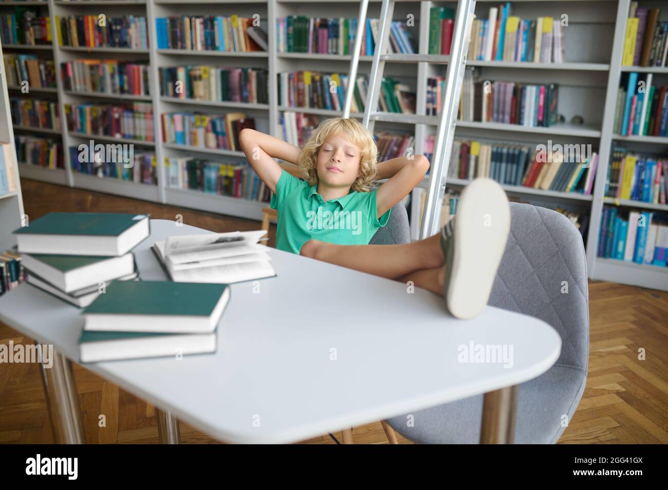 Simpatico allievo biondo che schizza in una biblioteca pubblica Foto Stock