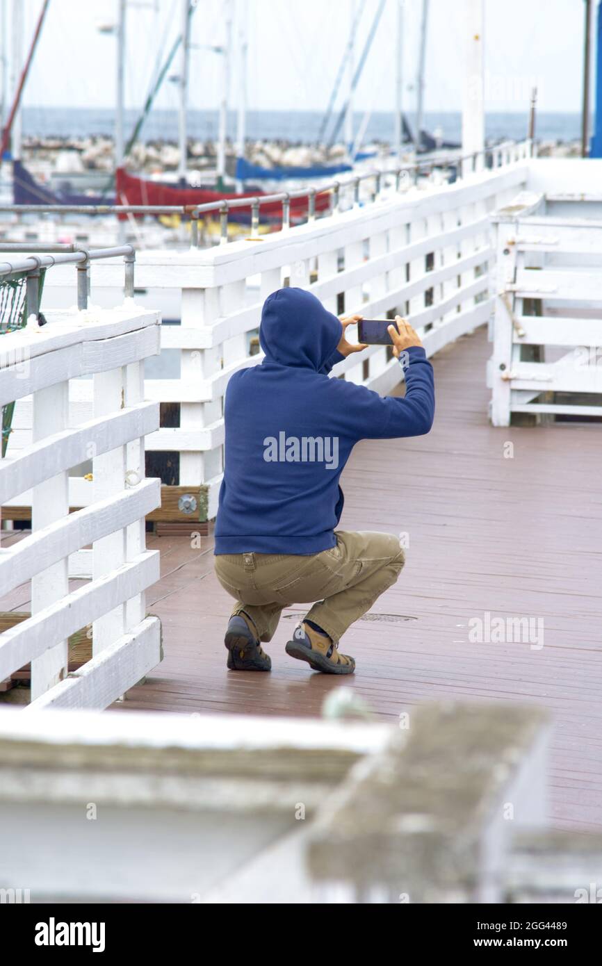 Uomo accovacciato e irriconoscibile con un cappuccio che parla l'immagine del porto Foto Stock