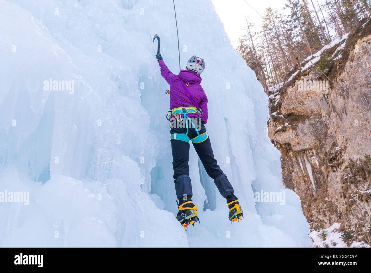 Arrampicata femminile su ghiaccio sul lato di un pendio ghiacciato con dossi, creste e iciclette Foto Stock