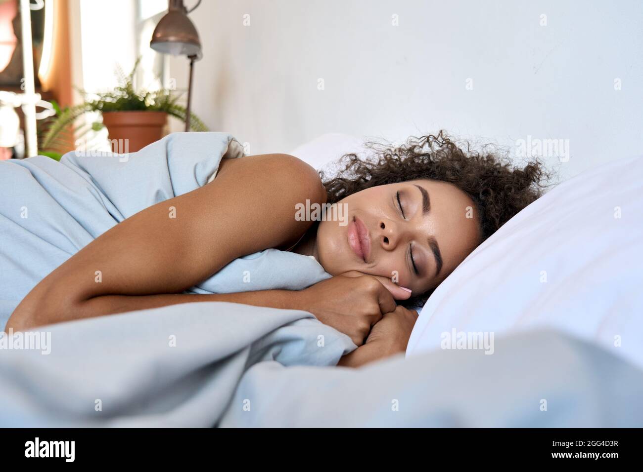 Giovane afroamericana che dorme in camera da letto moderna con gli occhi chiusi. Foto Stock