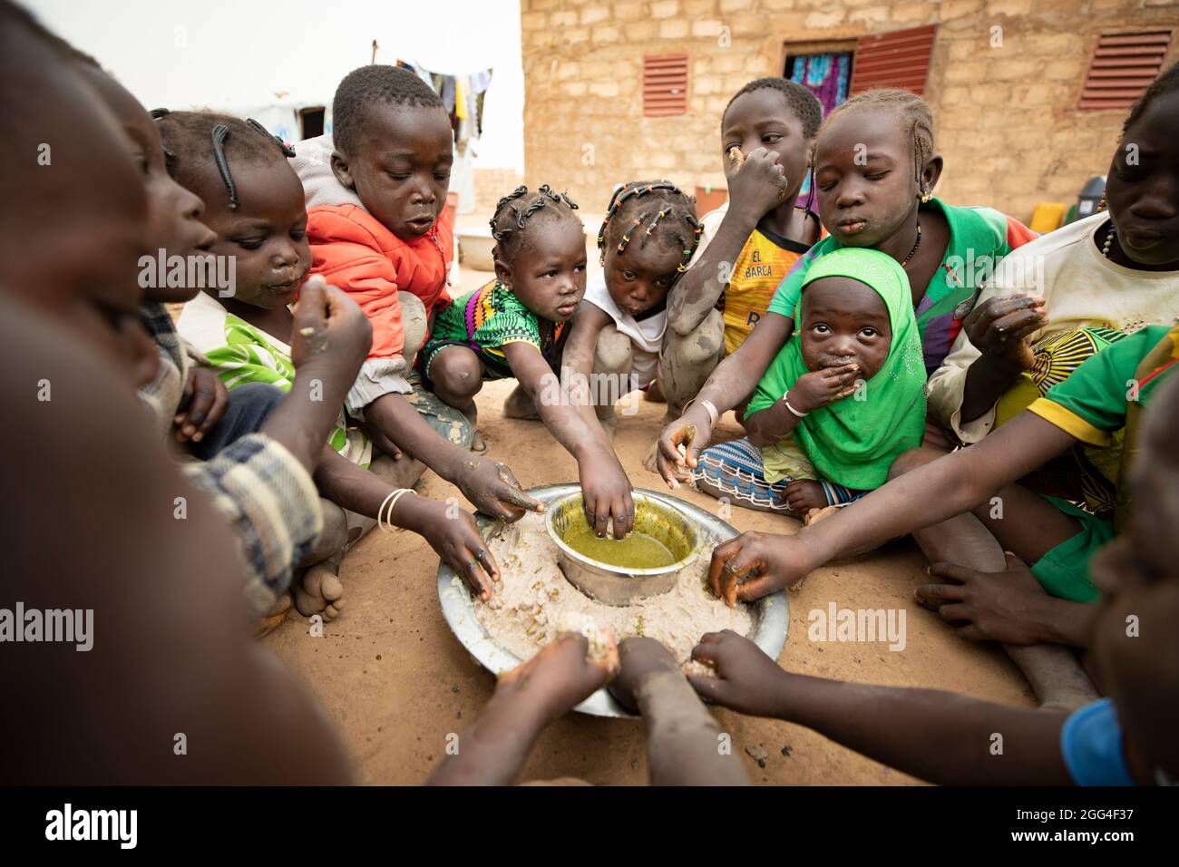 Un gruppo di bambini mangia intorno ad un piatto comune di pasta di miglio e stufato di foglie di baobab, probabilmente il loro unico pasto del giorno. Questa famiglia estesa è stata sfollata a causa della violenza e dell'insicurezza e ora si trova di fronte alla fame e alla carenza di cibo. Provincia di Kossi, Burkina Faso, Africa Occidentale. Foto Stock