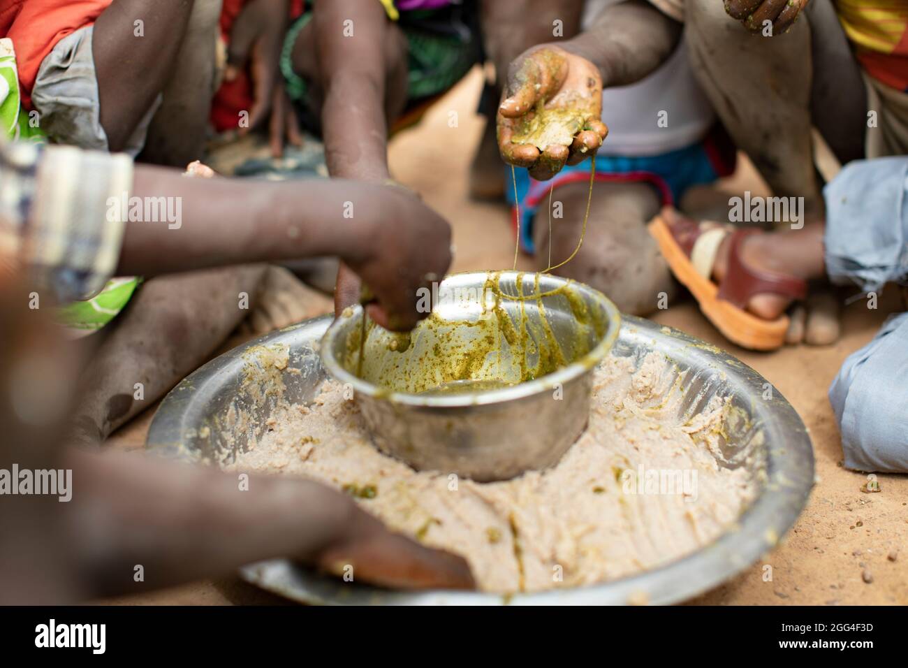 Un gruppo di bambini mangia intorno ad un piatto comune di pasta di miglio e stufato di foglie di baobab, probabilmente il loro unico pasto del giorno. Questa famiglia estesa è stata sfollata a causa della violenza e dell'insicurezza e ora si trova di fronte alla fame e alla carenza di cibo. Provincia di Kossi, Burkina Faso, Africa Occidentale. Foto Stock