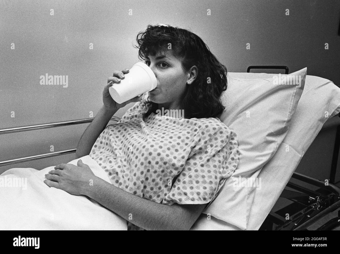 Austin Texas USA, circa 1990: Paziente ospedale femminile beve acqua per lavare i liquidi di prova utilizzati per test medici. ©Bob Daemmrich Foto Stock