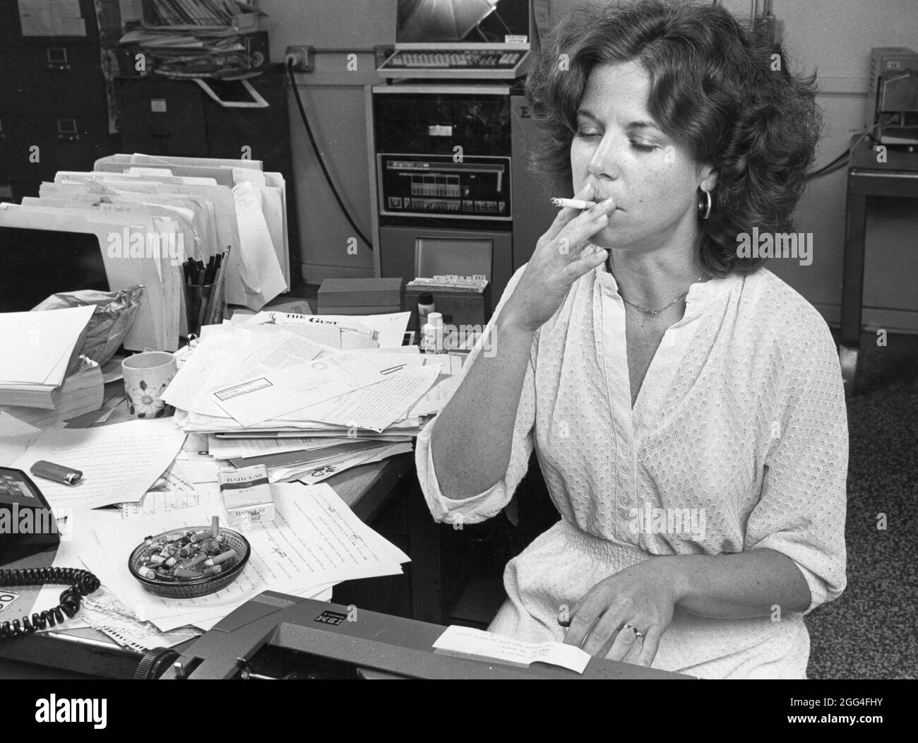 Austin Texas USA, circa 1984: Giornalista femminile che fuma sigaretta nella newsroom del giornale mentre si avvicina la scadenza. ©Bob Daemmrich Foto Stock