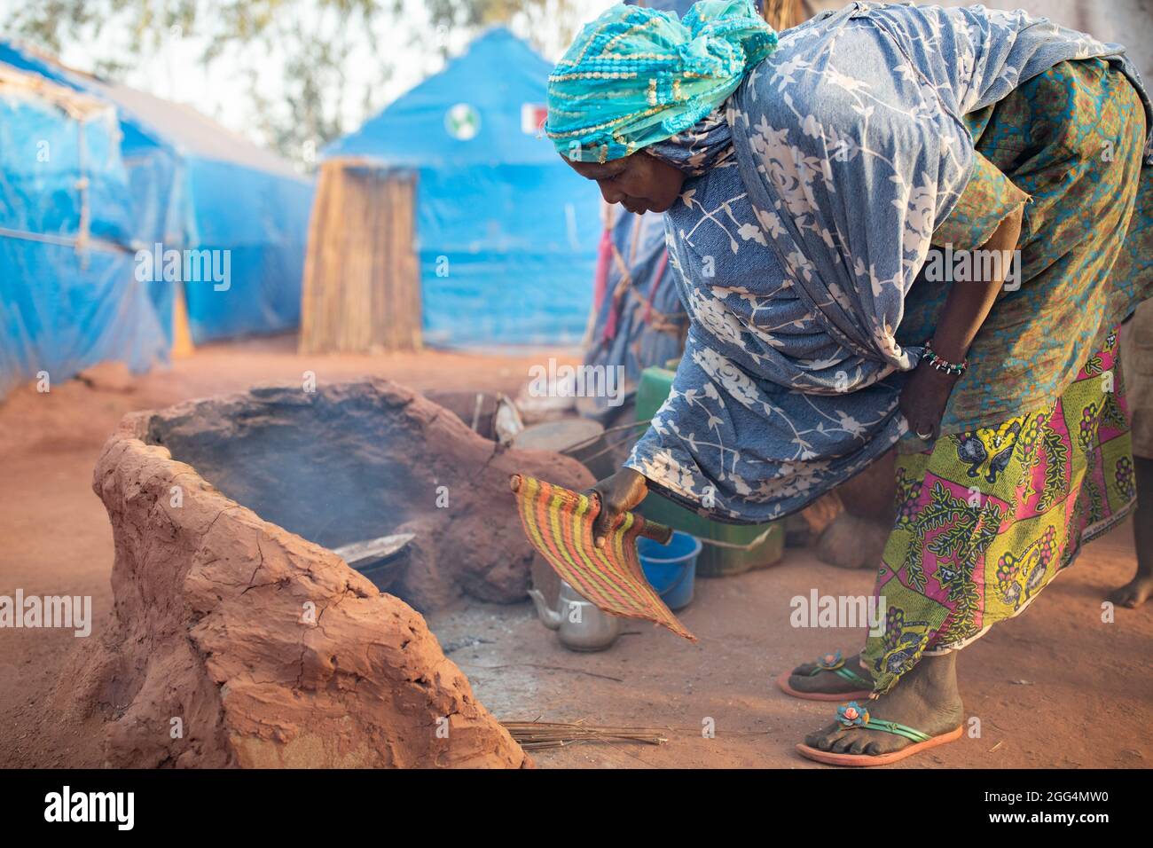 Il Senou Camp si trova al confine meridionale di Bamako, la capitale del Mali. Si tratta di uno degli otto campi informali della città e, di per sé, ospita 223 famiglie e poco più di 1.000 sfollati interni. Le famiglie che vivono qui sono fuggite dalla violenza e dall'insurrezione nella parte settentrionale e centrale del paese. Poiché la maggior parte di loro non ha mezzi di reddito o una normale fonte di cibo, la fame è una sfida quotidiana e la malnutrizione tra la sua popolazione continua ad essere diffusa. Qui, Miriam Barry tifosi un fuoco prima di cucinare la colazione per la sua famiglia fuori dal loro rifugio di fortuna al mattino. Foto Stock
