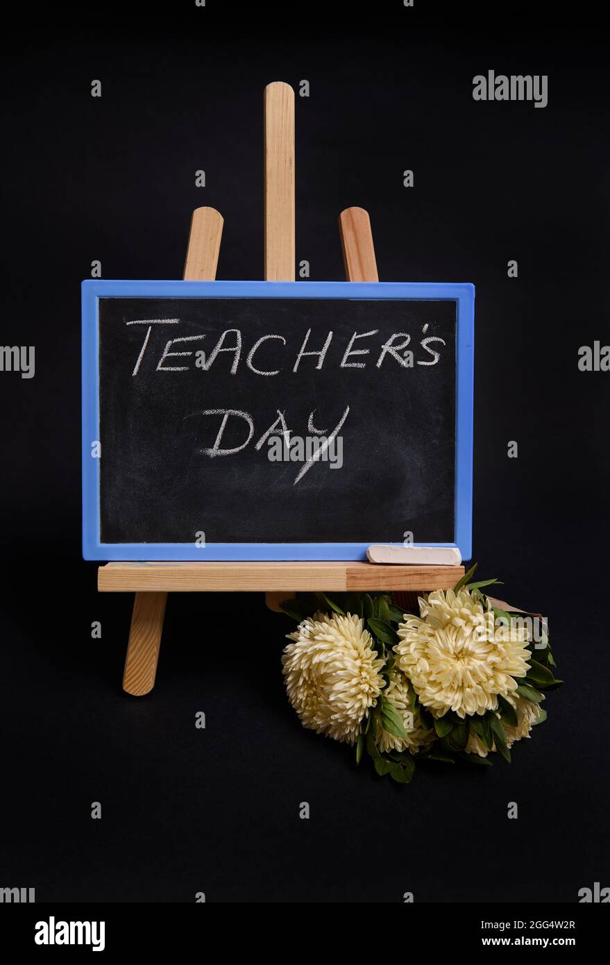 Primo piano di un bouquet di fiori di cerotti accanto a un lavagna di gesso con lettere Teachers Day, in piedi su un cavalletto in legno da tavolo, isolato su una ba nera Foto Stock