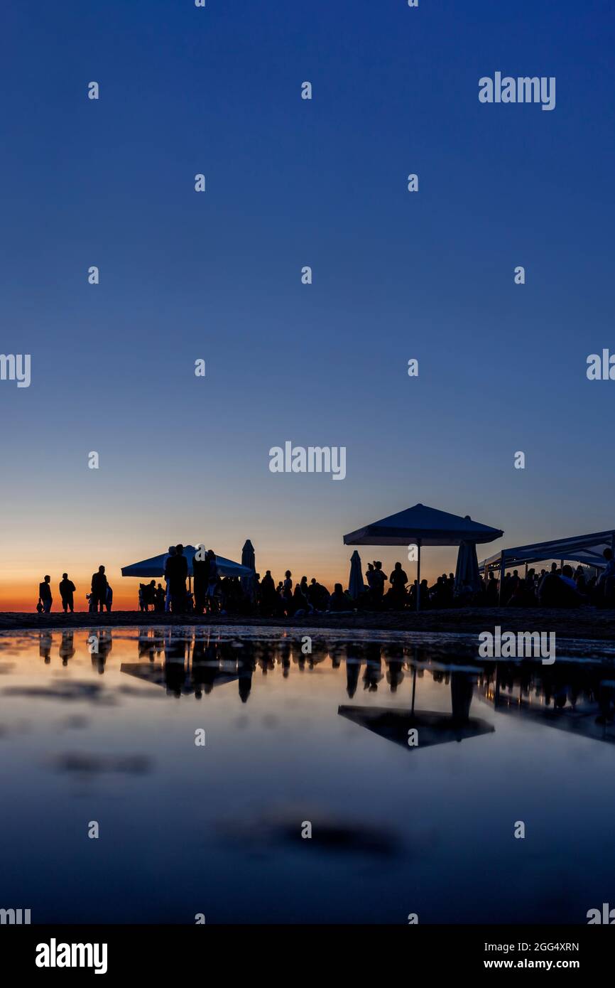 Sagome di una grande folla di gente al bar sul mare durante il tramonto con riflessi nell'acqua Foto Stock