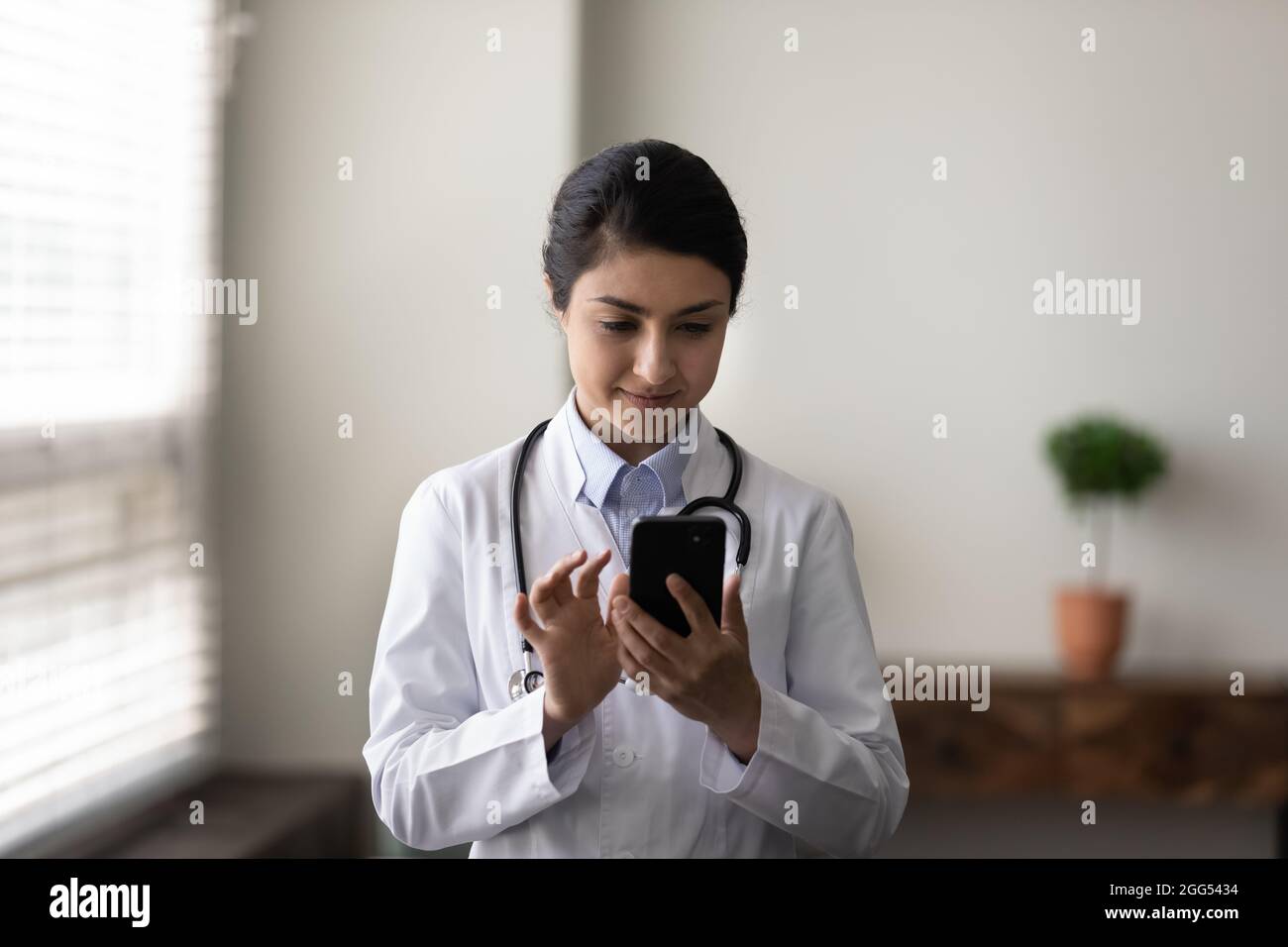 Felice giovane donna medico indiano utilizzando l'applicazione software mobile. Foto Stock