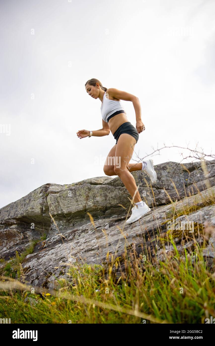 Vista laterale della donna che fa il running ad alta intensità sul fianco della montagna Foto Stock
