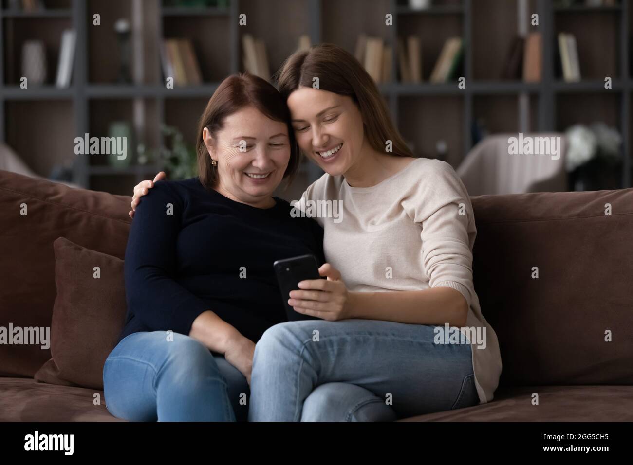 Giovane donna felice usando il cellulare con la madre più anziana. Foto Stock