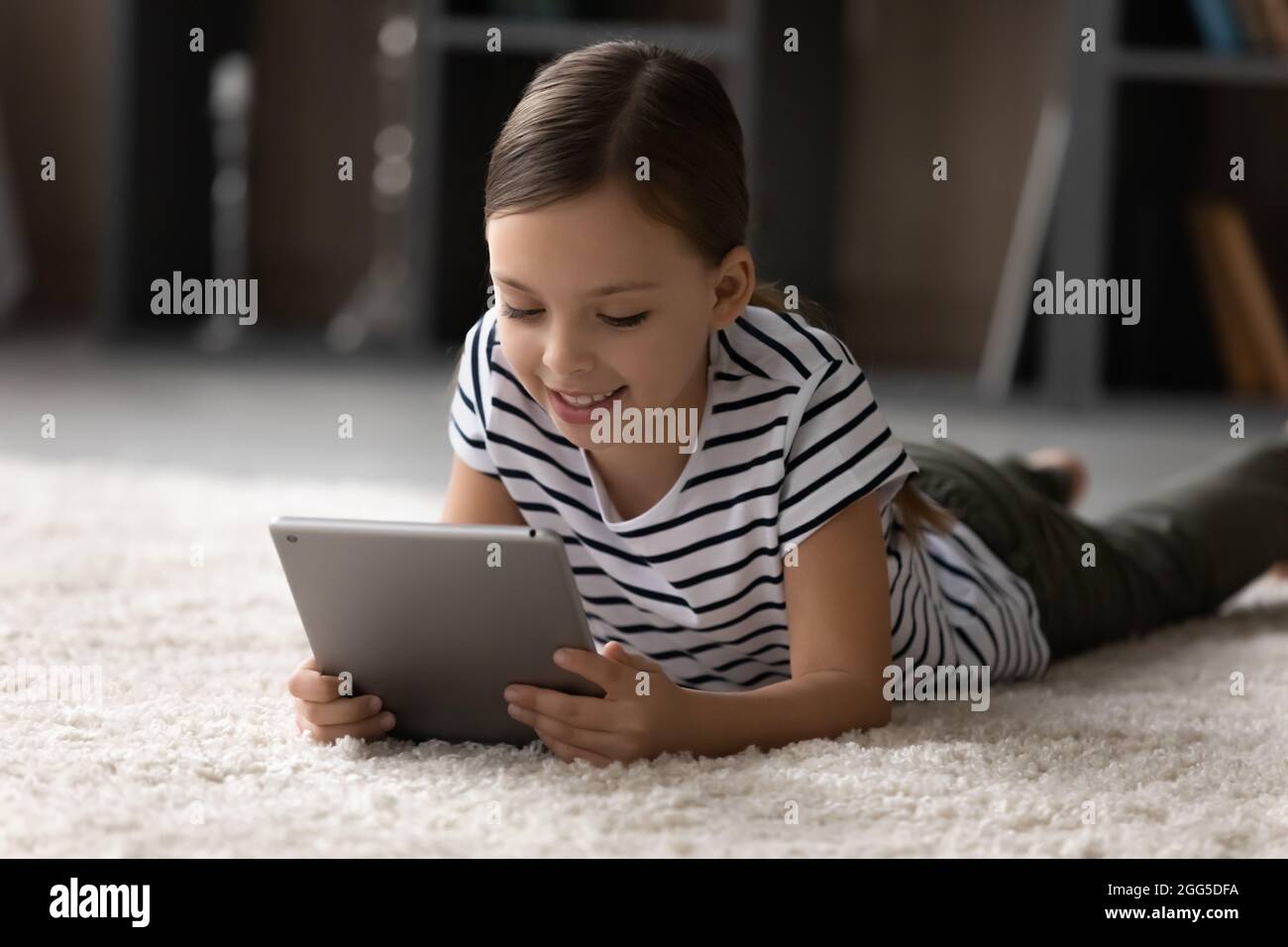 Ragazza carina felice che gioca sul tablet a casa. Foto Stock