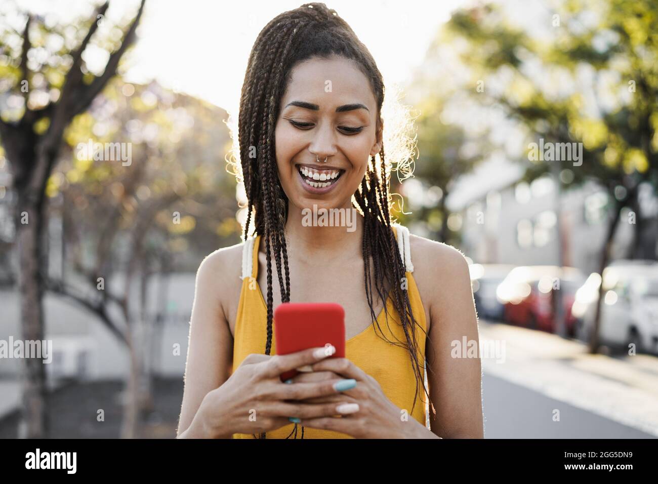 Bohemian ragazza mista corsa utilizzando il telefono cellulare all'aperto con la città in background - Focus on Face Foto Stock