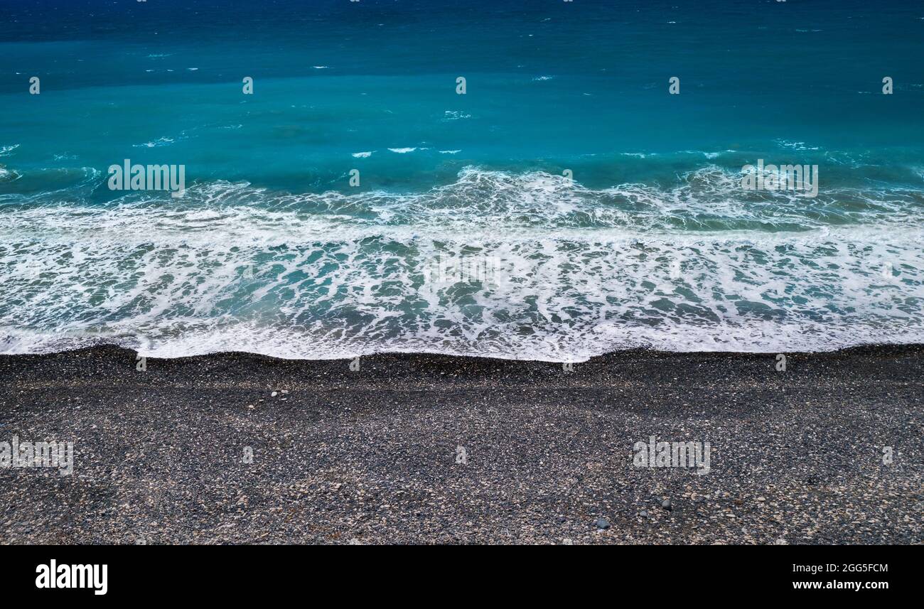 Sfondo marino con sabbia nera e ciottoli e onda di rottura, prospettiva ad angolo alto Foto Stock