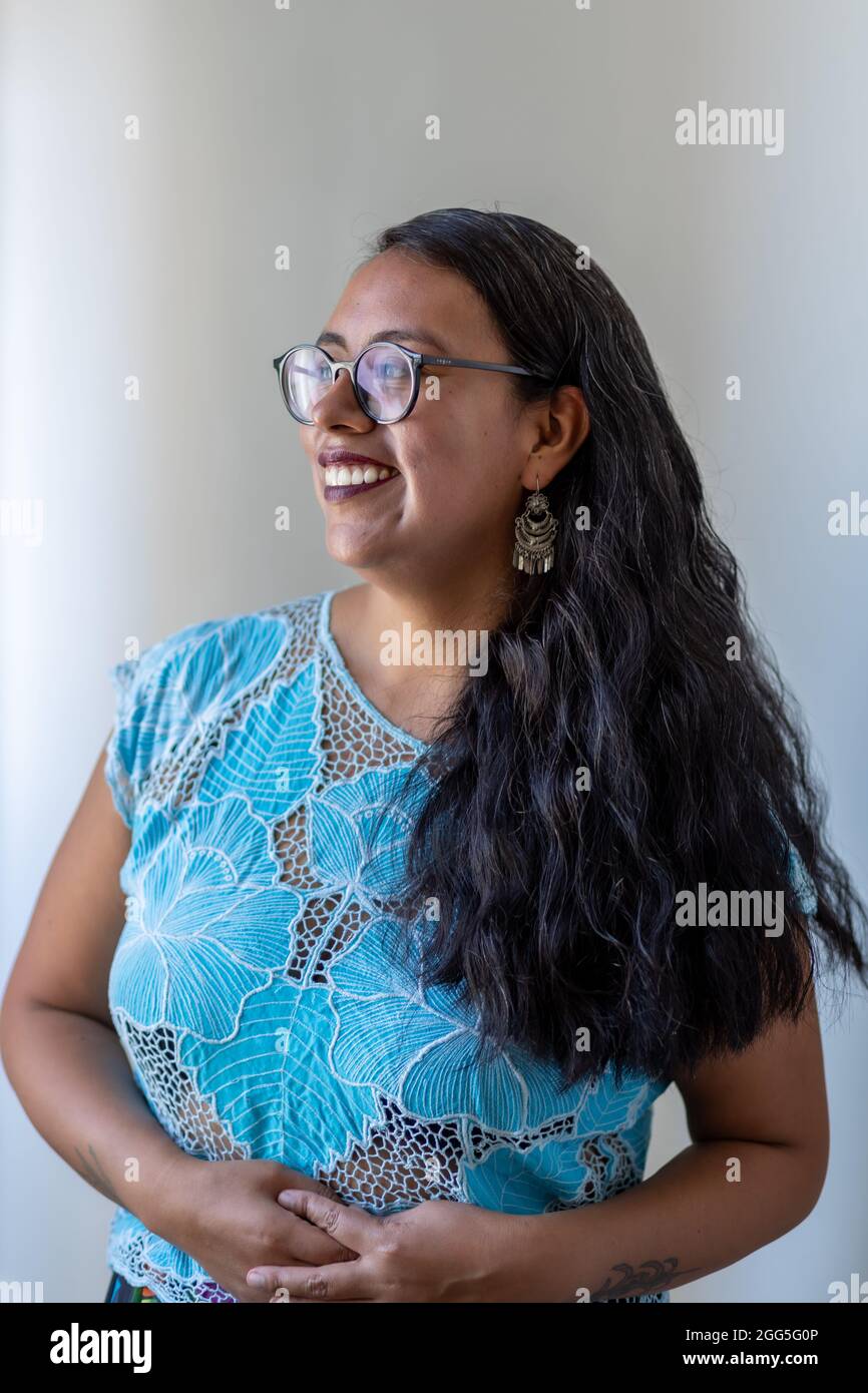 Un colpo verticale di una femmina ispanica sorridente che indossa una camicia blu con design floreale Foto Stock